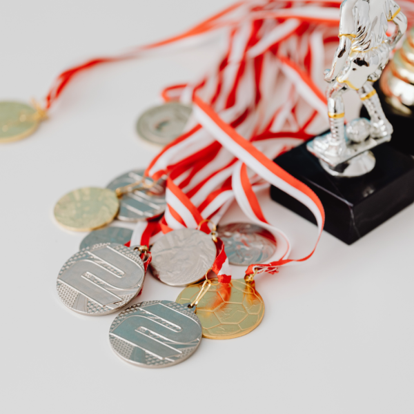 Uz balta fona redzamas sudraba un zelta medaļas ar sarkanbaltām lentēm