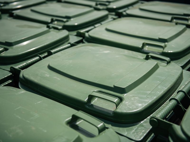 Daudzi zaļi plastmasas atkritumu konteineru vāki izvietoti rindās, redzami tuvplānā.