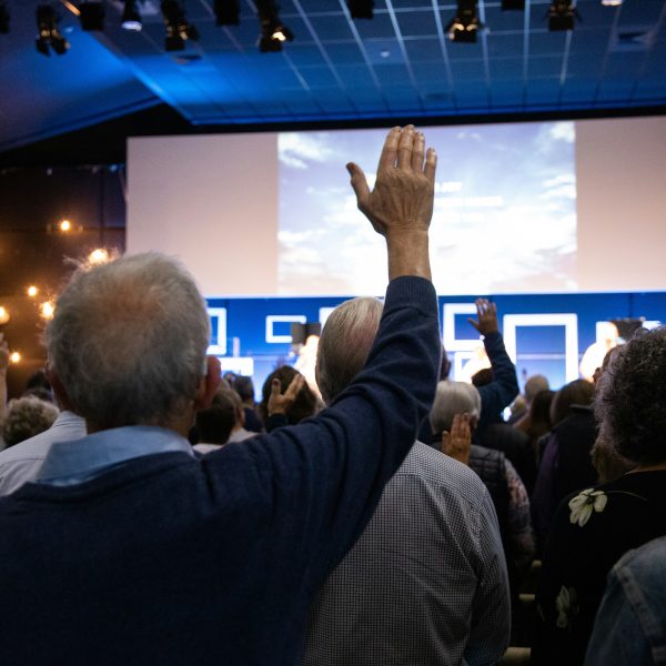 Cilvēku pūlis sanāksmju zālē, daudziem ir paceltas rokas. Viņi skatās uz lielu ekrānu. Mācības senioriem.