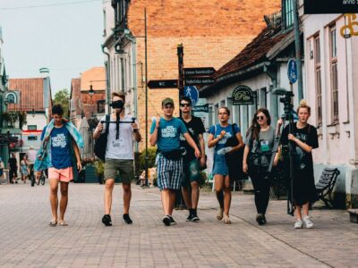 Seši jauni cilvēki iet pa bruģētu pilsētas ielu. Daži valkā T-kreklus ar uzrakstu "MEDIA SHARKS", un viens valkā T-kreklu ar uzrakstu "BAUNPILS". Divi no viņiem nes mediju aprīkojumu: viens tur kameras stabilizatoru, otrs – lielu statīvu ar mikrofonu. Fona ēkām ir vecas fasādes, un uz vienas ir uzraksts "SALONFRIZĒTAVA RITA anno 1964". Ielu zīme norāda uz "Annas baznīca 0.3", "WC 0.1", "Viegli uzliekas mašīna" un "BAUNPILS".