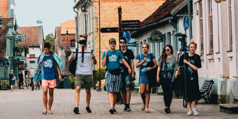 Seši jauni cilvēki iet pa bruģētu pilsētas ielu. Daži valkā T-kreklus ar uzrakstu "MEDIA SHARKS", un viens valkā T-kreklu ar uzrakstu "BAUNPILS". Divi no viņiem nes mediju aprīkojumu: viens tur kameras stabilizatoru, otrs – lielu statīvu ar mikrofonu. Fona ēkām ir vecas fasādes, un uz vienas ir uzraksts "SALONFRIZĒTAVA RITA anno 1964". Ielu zīme norāda uz "Annas baznīca 0.3", "WC 0.1", "Viegli uzliekas mašīna" un "BAUNPILS".